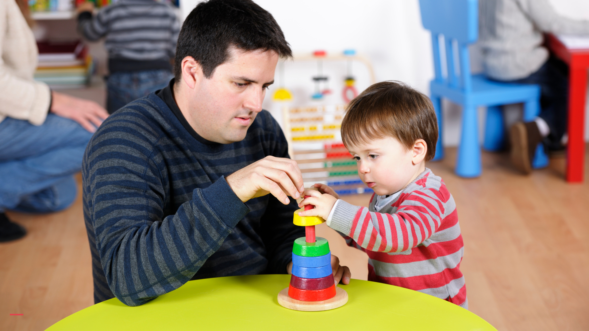 Un éducateur de la petite enfance aide un jeune enfant à empiler des anneaux colorés cap aepe paris