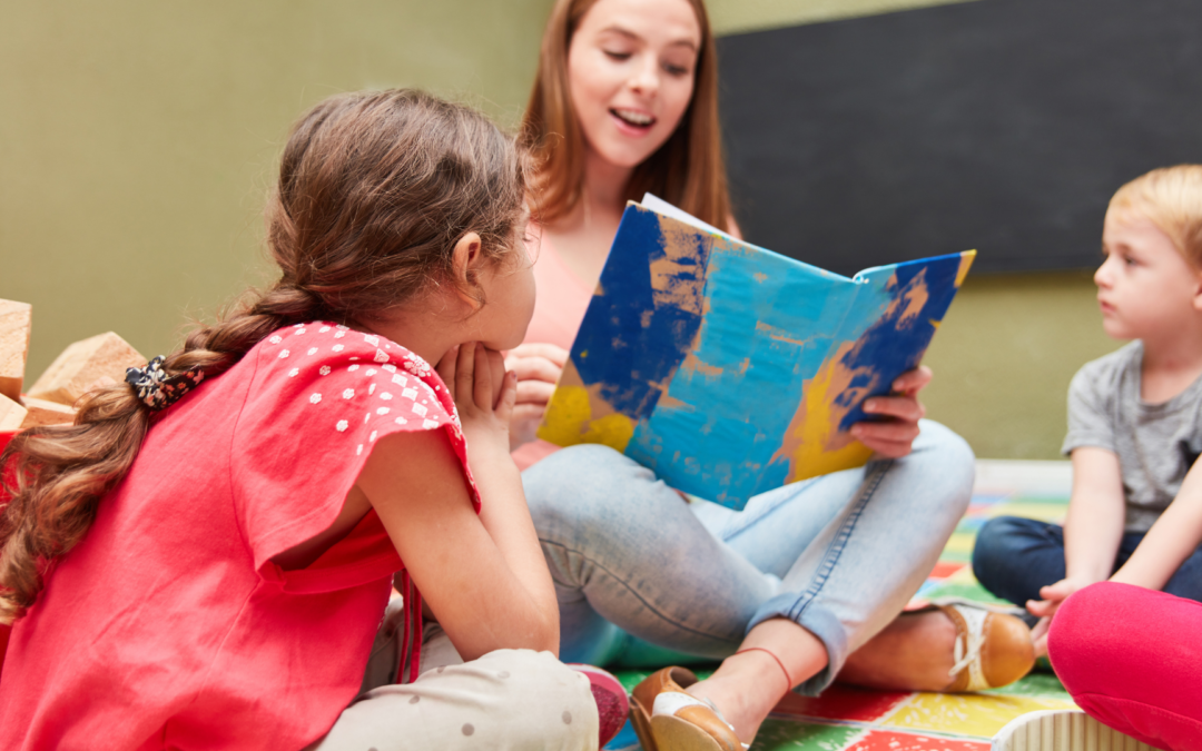 Une éducatrice lit une histoire à un groupe de jeunes enfants, assis en cercle, dans une salle de classe colorée