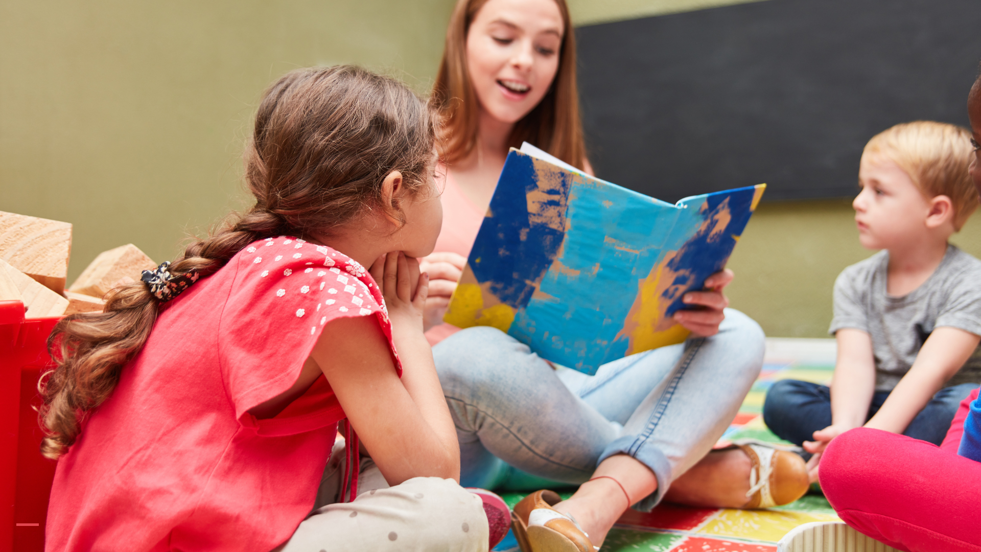 Une éducatrice lit une histoire à un groupe de jeunes enfants, assis en cercle, dans une salle de classe colorée